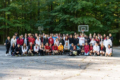 A large group of students pose for a photo near a wooden area.